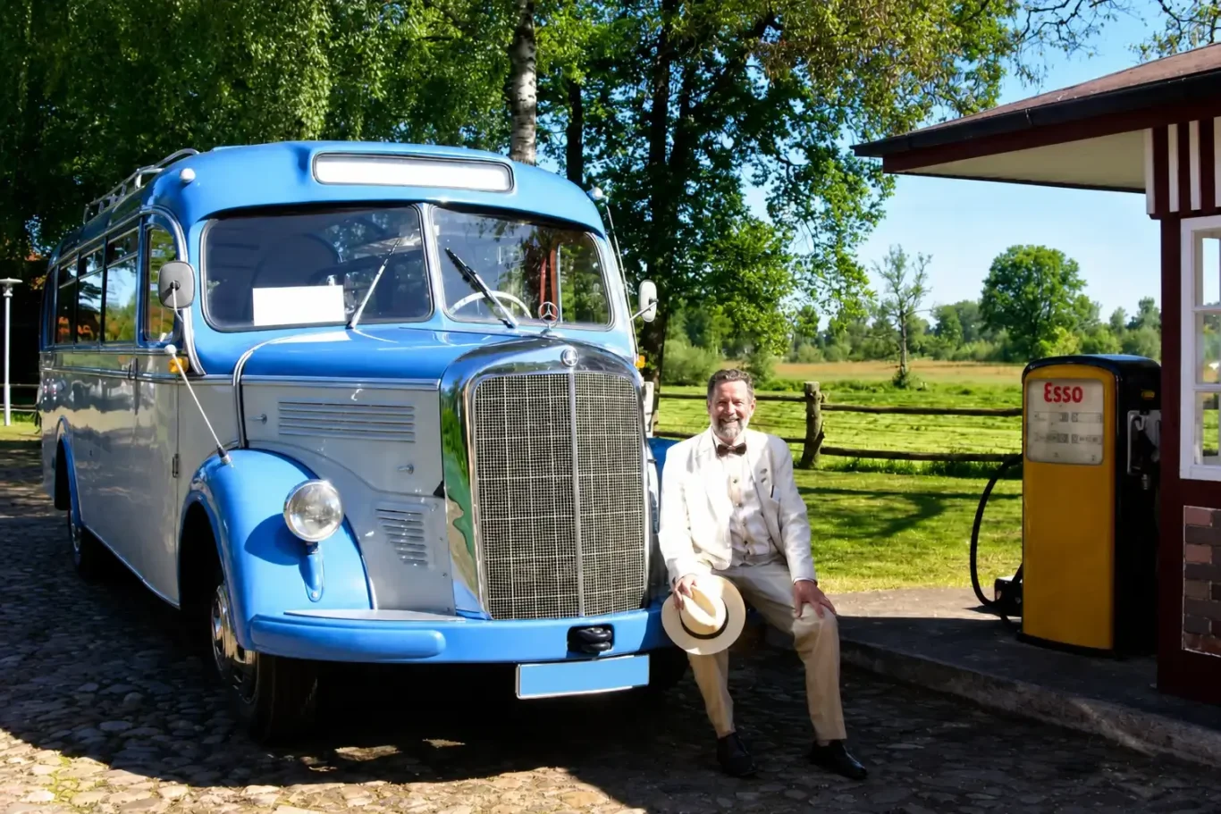 Chauffeur sitzt auf der Stoßstange eines blauen Oldtimerbusses